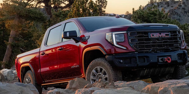 Red GMC Sierra pickup truck on a rugged rocky trail at sunset.